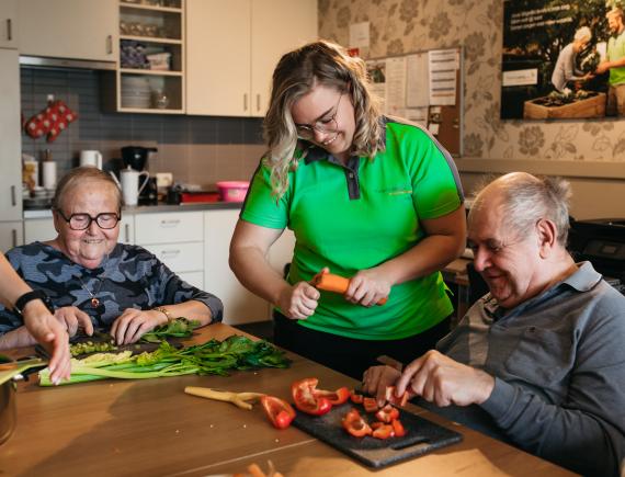 Verzorgende van Familiezorg O-Vl. helpt twee oudere mannen tijdens het koken.