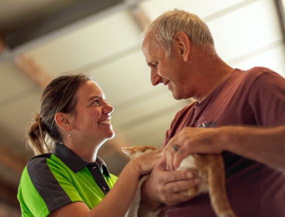 Verzorgende van Familiezorg O-Vl. kijkt mannelijke cliënt met jongdementie in de ogen terwijl hij een katje in de armen neemt en streelt.