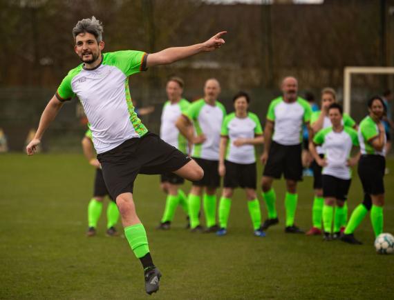 Een medewerker van Familiezorg in voetbaloutfit schopt een voetbal naar de goal.